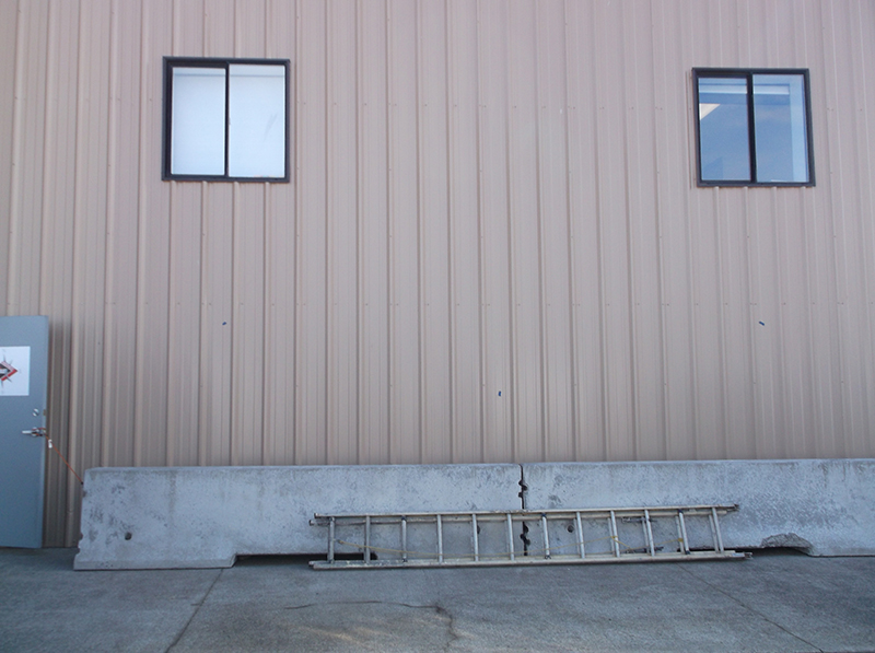 Side of metal paneling industrial building at Brooklane building | Long concrete barriers along wall