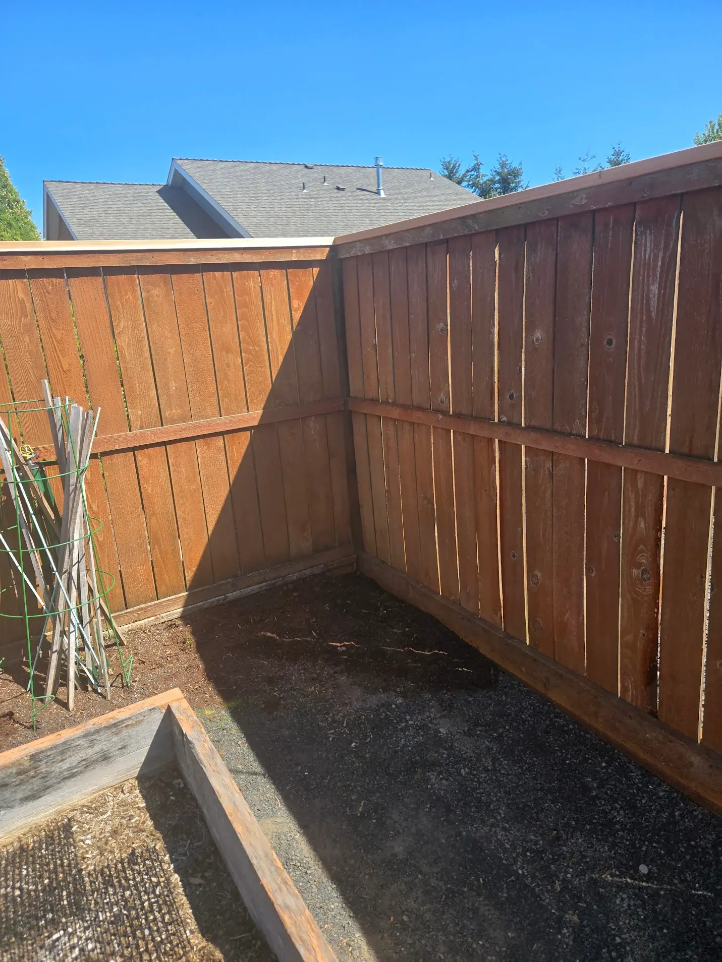 Corner of a cedar fence with midline wooden horizontal piece and fence cap along top.